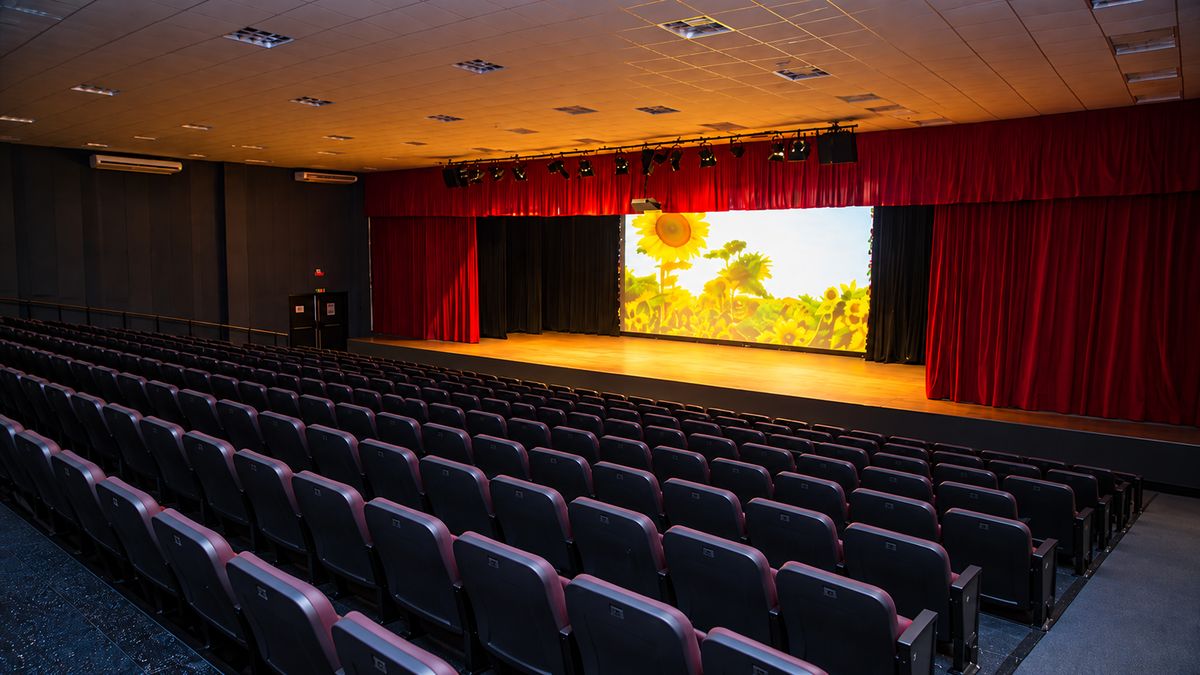 Auditório da Arena de Eventos de Santana de Parnaíba com plateia de poltronas vermelhas e palco iluminado por uma projeção de girassóis