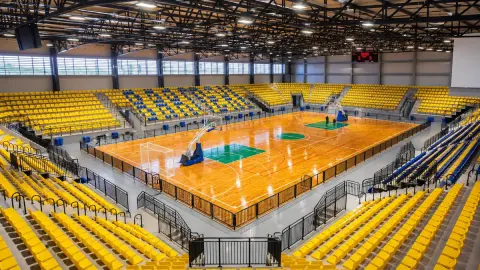 Ginásio do Complexo Esportivo do Jardim Silveira, em Barueri, com quadra de madeira, arquibancadas amarelas e azuis, traves de futsal, cestas de basquete e placar eletrônico.