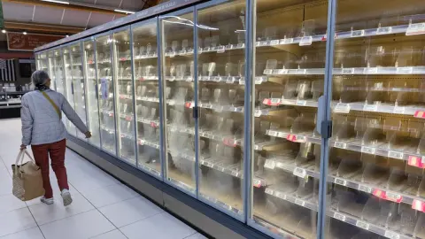 Geladeiras de supermercado vazias na França, com uma cliente caminhando ao lado dos expositores