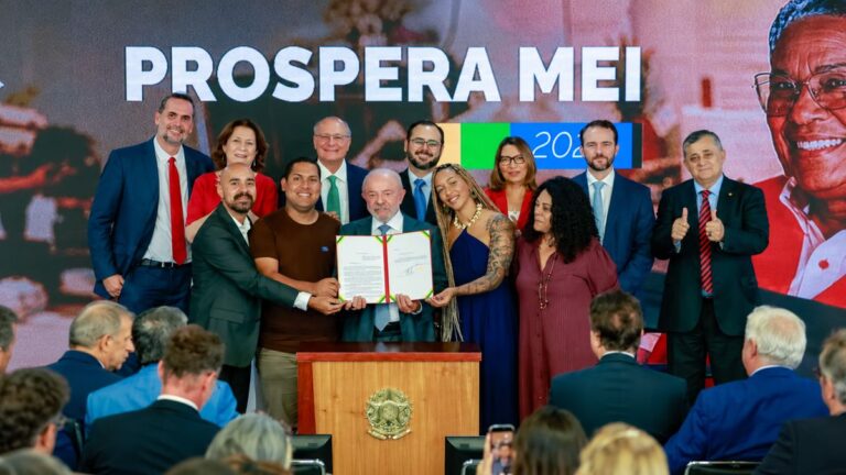 Lula segura decreto assinado ao lado de microempreendedores no Palácio do Planalto, com painel Prospera MEI ao fundo