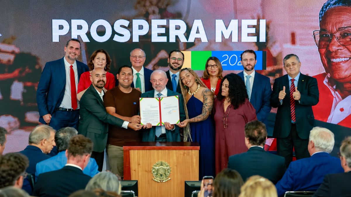 Lula segura decreto assinado ao lado de microempreendedores no Palácio do Planalto, com painel Prospera MEI ao fundo